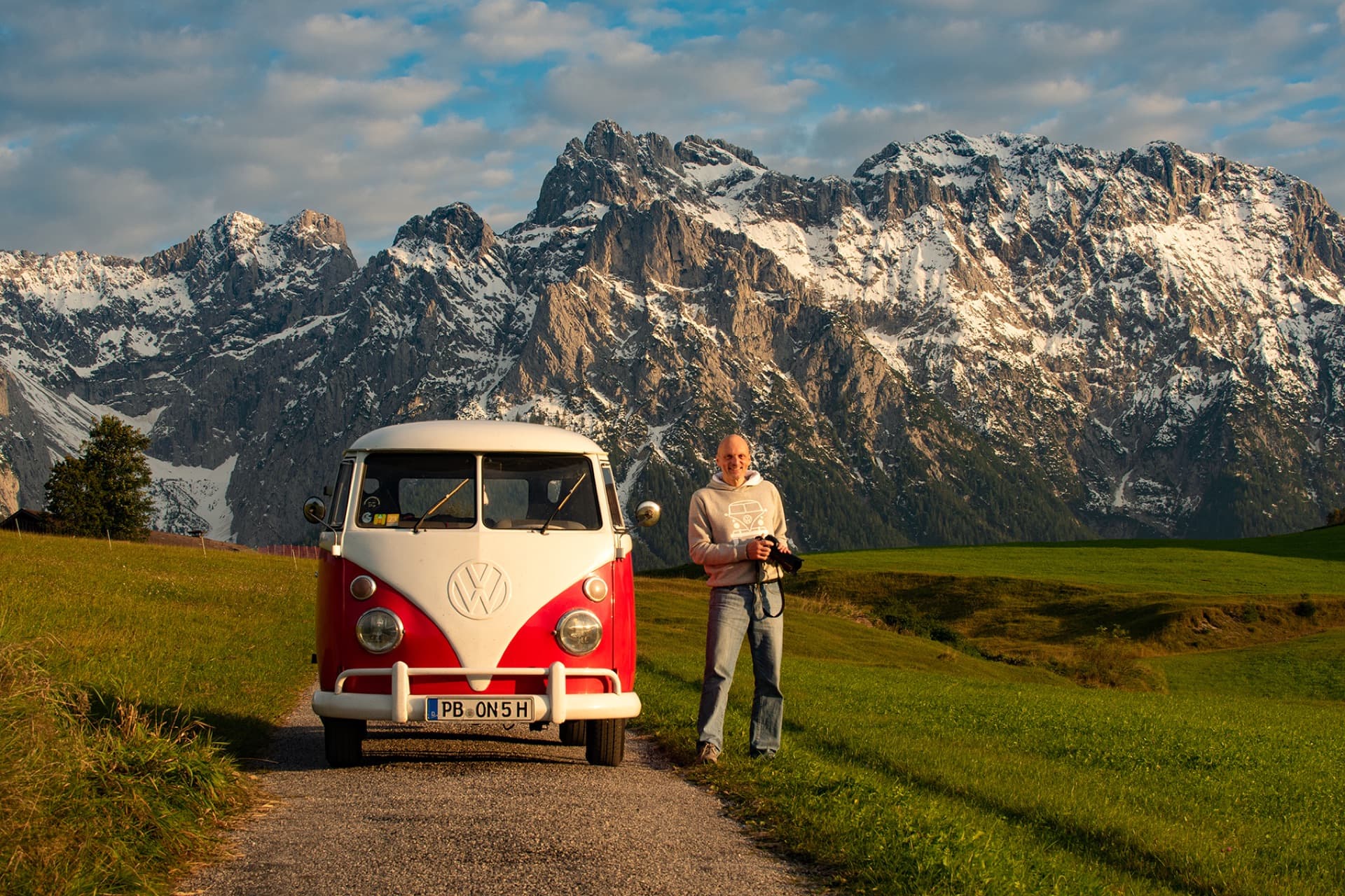 Peter Gebhard steht mit seinem rot-weißen VW Bulli vor einer Bergkulisse